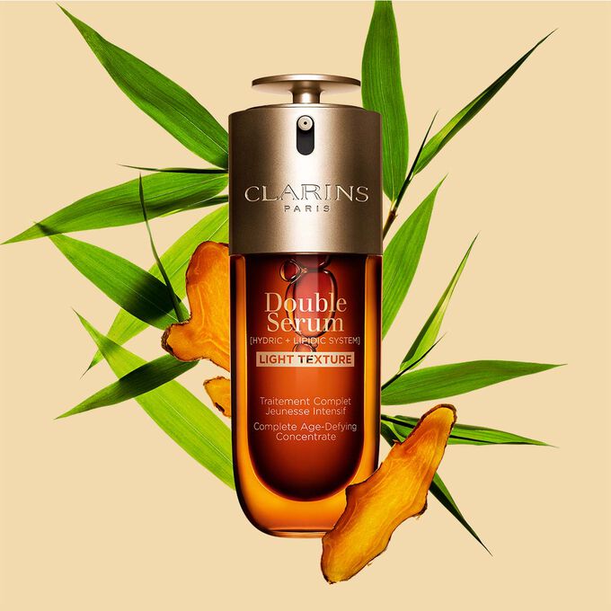 ขวด Clarins Double Serum Light Texture ขนาด 50 มล.วางอยู่ท่ามกลาง Turmeric และใบ Provençal Reed บนพื้นหลังสีส้ม