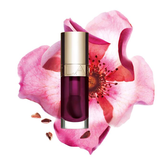 ภาพถ่ายผลิตภัณฑ์ Clarins Lip Comfort Oil Plum วางอยู่ข้าง Sweetbriar Rose บนพื้นหลังสีชมพูอ่อน