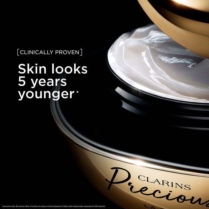 ภาพผลิตภัณฑ์ Clarins Precious Soft Cream บนพื้นหลังสีเข้มพร้อมข้อความที่เน้นถึงประสิทธิภาพในการช่วยให้ผิวดูอ่อนเยาว์ลง 5 ปี
