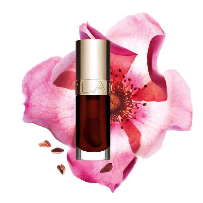 ภาพถ่ายผลิตภัณฑ์ Clarins Lip Comfort Oil Chocolate วางอยู่ข้าง Sweetbriar Rose บนพื้นหลังสีชมพูอ่อน