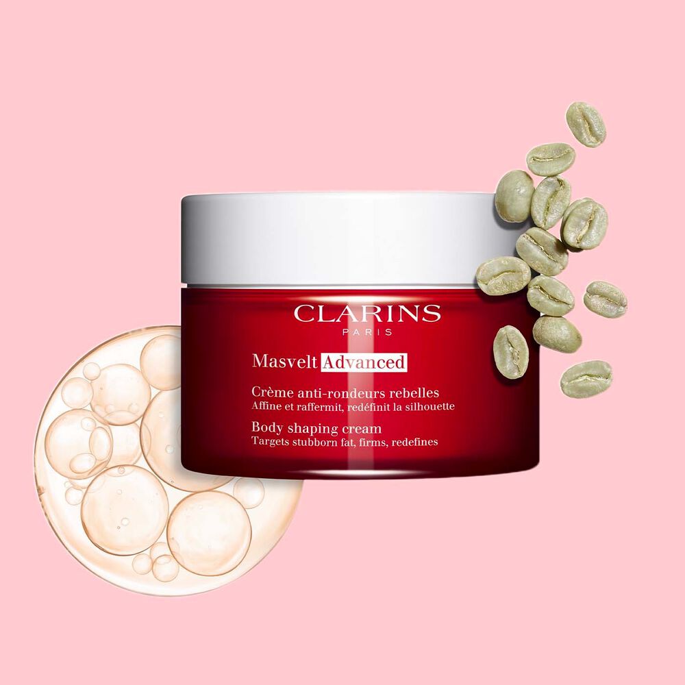 การถ่ายภาพผลิตภัณฑ์ Clarins Masvelt Advanced Body Contouring Cream ที่วางข้างเมล็ดกาแฟบนพื้นหลังสีชมพูอ่อน เพื่อเน้นถึงส่วนผสมจากธรรมชาติและคุณสมบัติในการช่วยรักษารูปร่าง