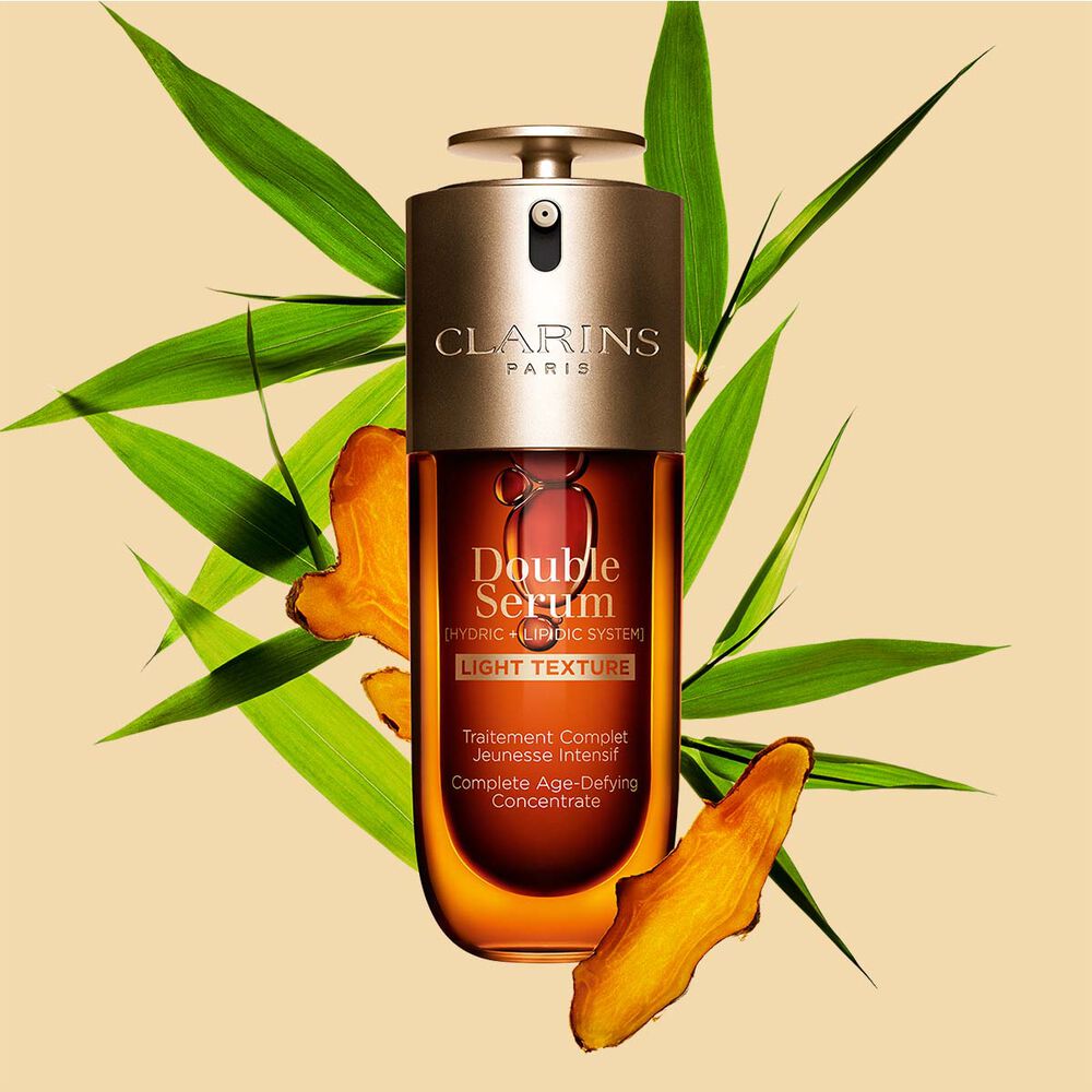 ขวด Clarins Double Serum Light Texture ขนาด 75 มล.วางอยู่ท่ามกลาง Turmeric และใบ Proven&ccedil;al Reed บนพื้นหลังสีส้ม