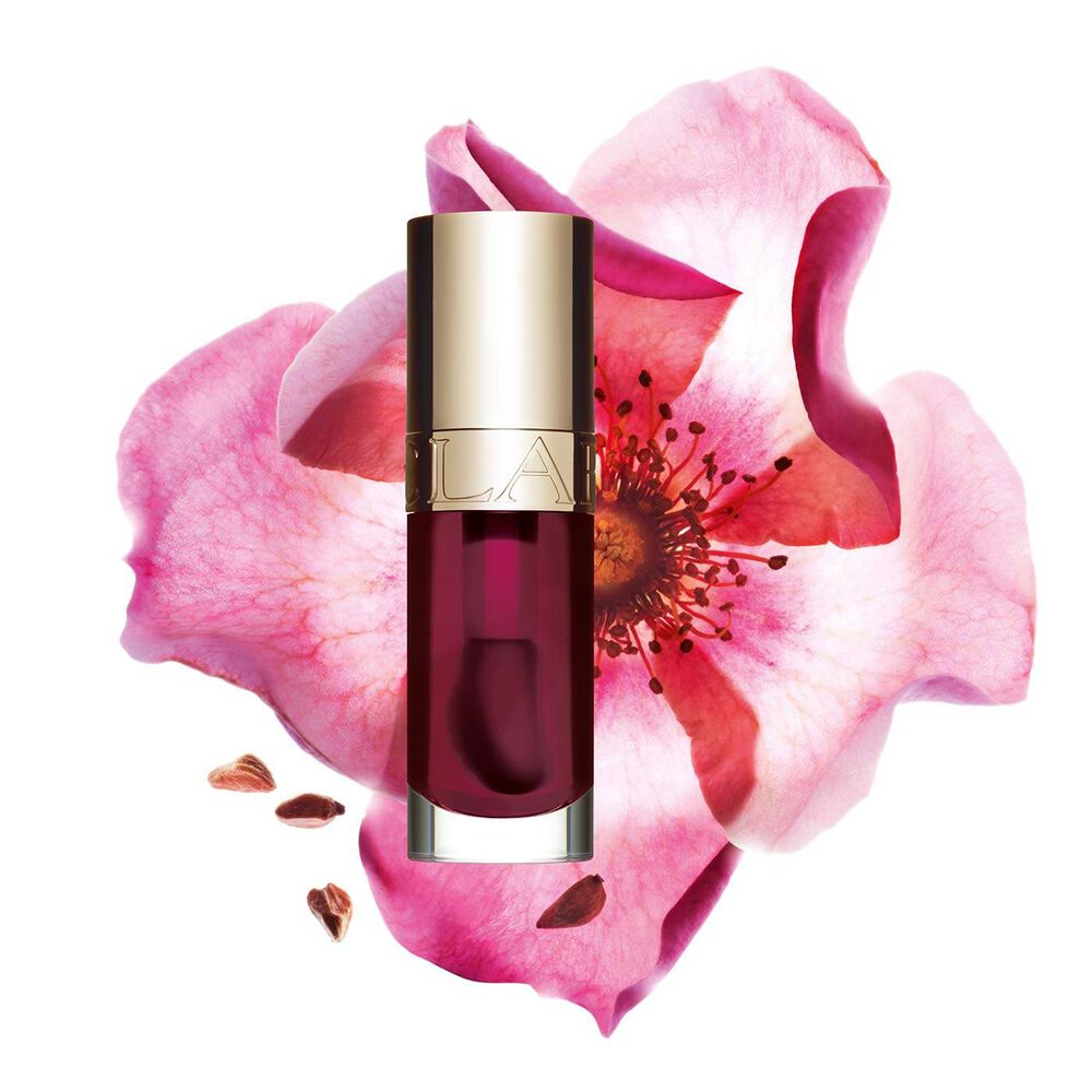 ภาพถ่ายผลิตภัณฑ์ Clarins Lip Comfort Oil Fig วางอยู่ข้าง Sweetbriar Rose บนพื้นหลังสีชมพูอ่อน
