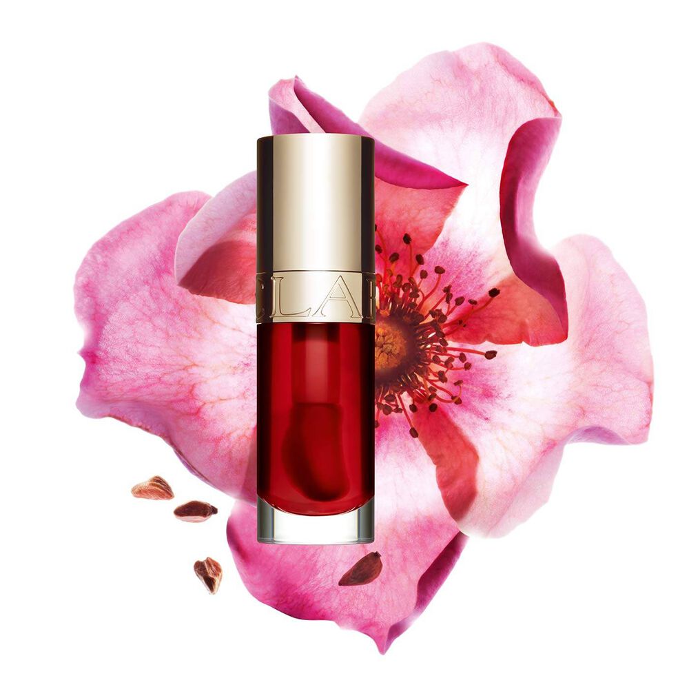 ภาพถ่ายผลิตภัณฑ์ Clarins Lip Comfort Oil Strawberry วางอยู่ข้าง Sweetbriar Rose บนพื้นหลังสีชมพูอ่อน