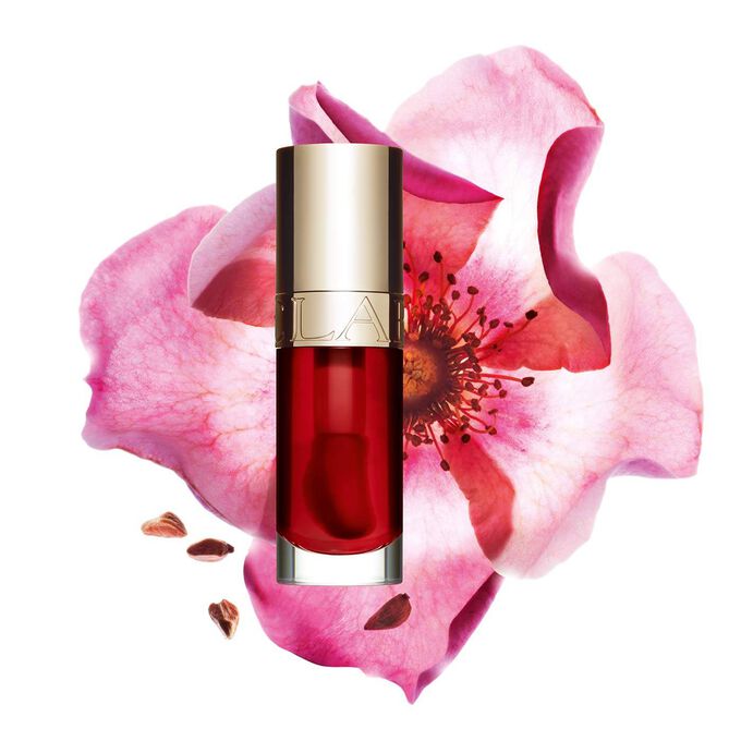 ภาพถ่ายผลิตภัณฑ์ Clarins Lip Comfort Oil Strawberry วางอยู่ข้าง Sweetbriar Rose บนพื้นหลังสีชมพูอ่อน