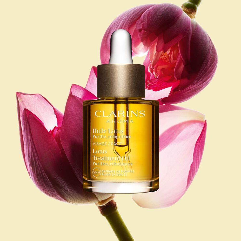 ภาพผลิตภัณฑ์ของขวด Clarins Lotus Face Treatment Oil ที่วางอยู่ใกล้ดอกบัว บนพื้นหลังสีเหลืองอ่อน