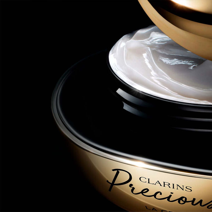 ภาพผลิตภัณฑ์ Clarins Precious Soft Cream บนพื้นหลังสีเข้มพร้อมข้อความที่เน้นถึงประสิทธิภาพในการช่วยให้ผิวดูอ่อนเยาว์ลง 5 ปี