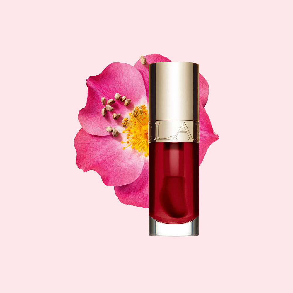 ภาพถ่ายผลิตภัณฑ์ Clarins Lip Comfort Oil สี Cherry วางอยู่ข้าง Sweetbriar Rose บนพื้นหลังสีชมพูอ่อน