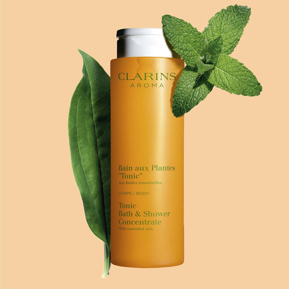 ภาพผลิตภัณฑ์ของ Clarins Tonic Bath และ Shower Concentrate ที่วางอยู่ใกล้กับใบสะระแหน่และโรสแมรี่บนพื้นหลังสีส้ม