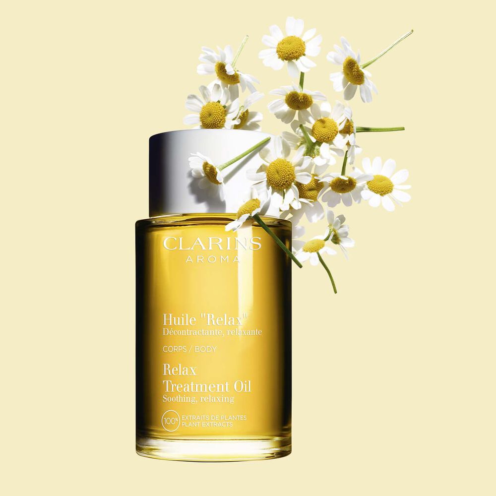 ภาพผลิตภัณฑ์ของขวด Clarins Relax Body Treatment Oil ที่วางอยู่ใกล้ช่อดอกคาโมมายล์ บนพื้นหลังสีเหลืองอ่อน