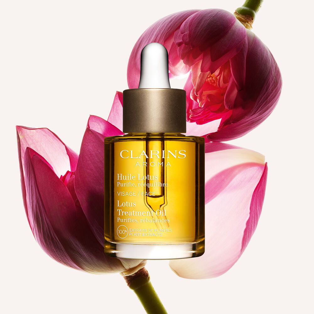 ภาพผลิตภัณฑ์ของขวด Clarins Lotus Face Treatment Oil ที่วางอยู่ใกล้ดอกบัว บนพื้นหลังสีเหลืองอ่อน