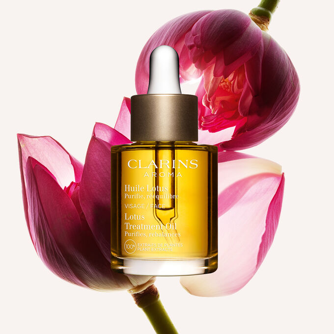 ภาพผลิตภัณฑ์ของขวด Clarins Lotus Face Treatment Oil ที่วางอยู่ใกล้ดอกบัว บนพื้นหลังสีเหลืองอ่อน
