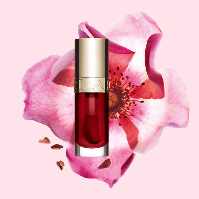 ภาพถ่ายผลิตภัณฑ์ Clarins Lip Comfort Oil สี Cherry วางอยู่ข้าง Sweetbriar Rose บนพื้นหลังสีชมพูอ่อน
