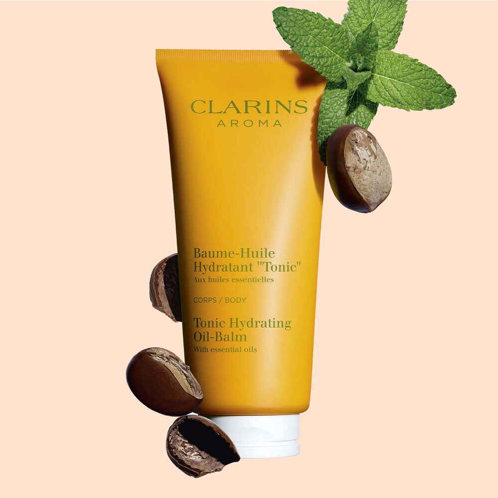 ภาพผลิตภัณฑ์ของบรรจุภัณฑ์ Clarins Tonic Hydrating Oil-Balm ที่วางใกล้ใบมิ้นต์และเมล็ดเชีย บนพื้นหลังสีพีช