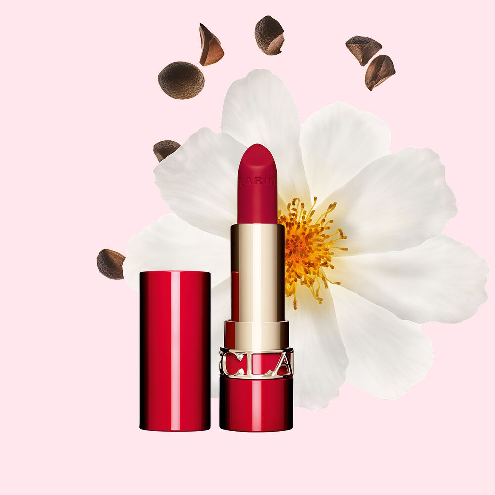 ภาพถ่ายผลิตภัณฑ์ Clarins Matte Lipstick Joli Rouge ในสี 742 V วางอยู่ข้างดอก Camellia และเมล็ดเชียบนพื้นหลังสีชมพู