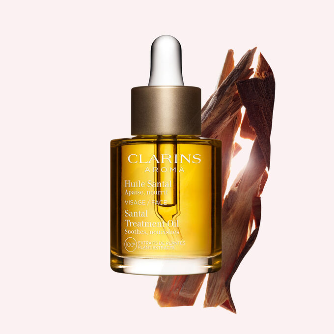 ภาพผลิตภัณฑ์ของขวด Clarins Santal Face Treatment Oil ที่วางใกล้กับเปลือกไม้จันทน์บนพื้นหลังสีเหลืองอ่อน
