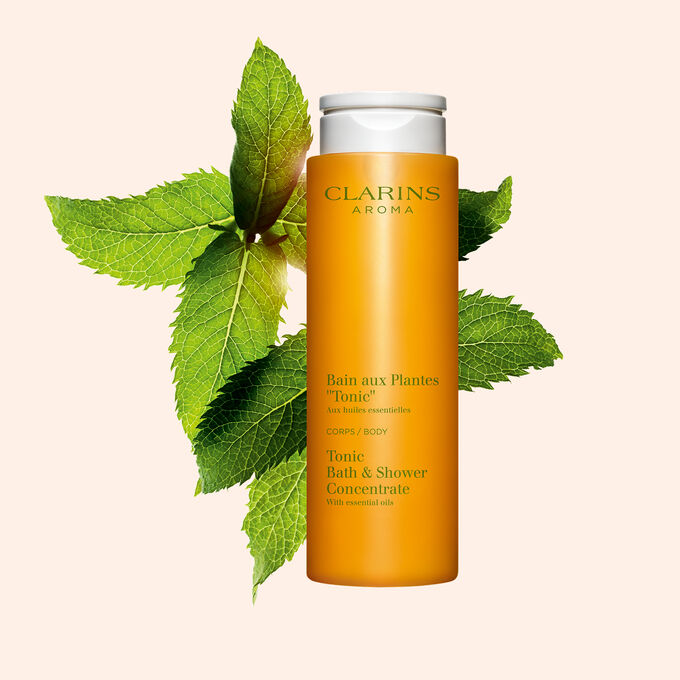 ภาพผลิตภัณฑ์ของ Clarins Tonic Bath และ Shower Concentrate ที่วางอยู่ใกล้กับใบสะระแหน่และโรสแมรี่บนพื้นหลังสีส้ม